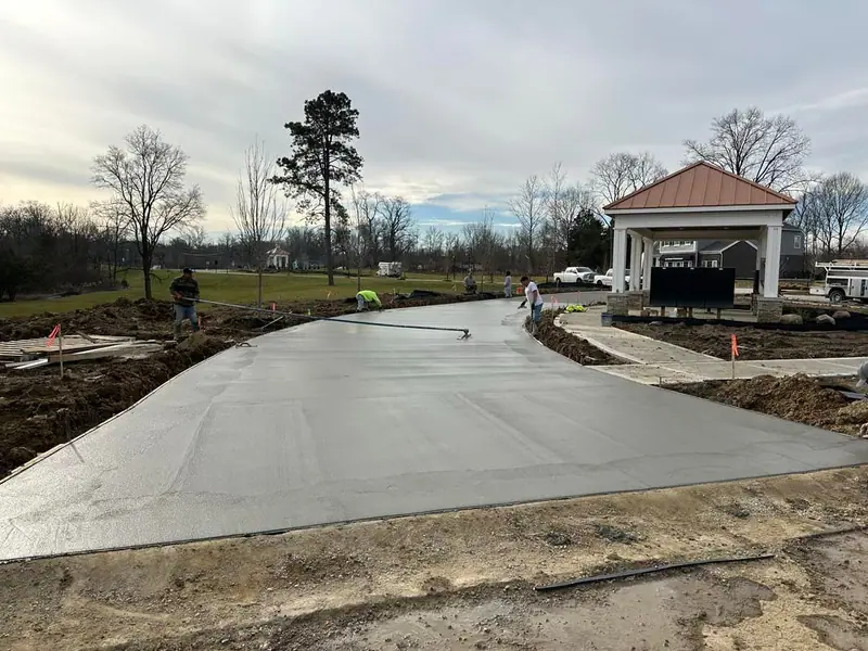 Crew finishing a newly poured curved concrete drive near a pavilion