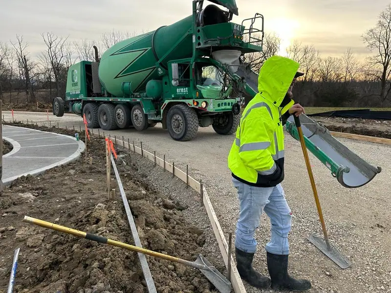 Pride Concrete crew member in a high-visibility jacket with a concrete mixer truck on a job site