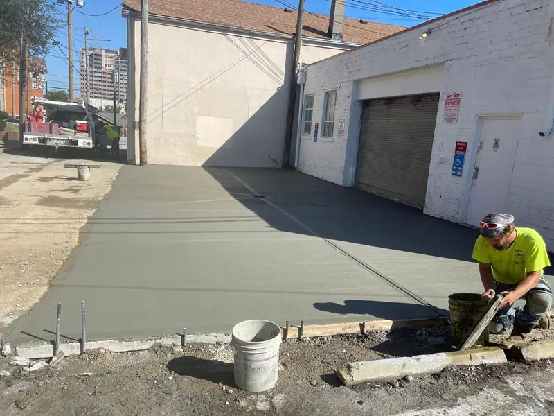 Worker finishing a concrete slab beside a garage
