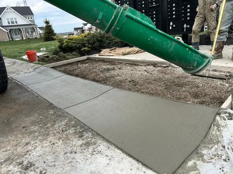 Concrete walk being poured from a mixer chute near a mailbox pad